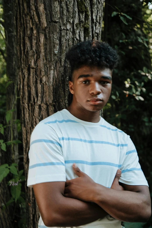 a young black man is standing by a tree