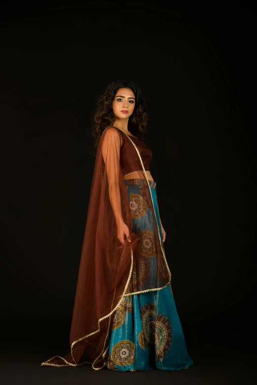 a woman posing for a po wearing a long blue dress and brown cape