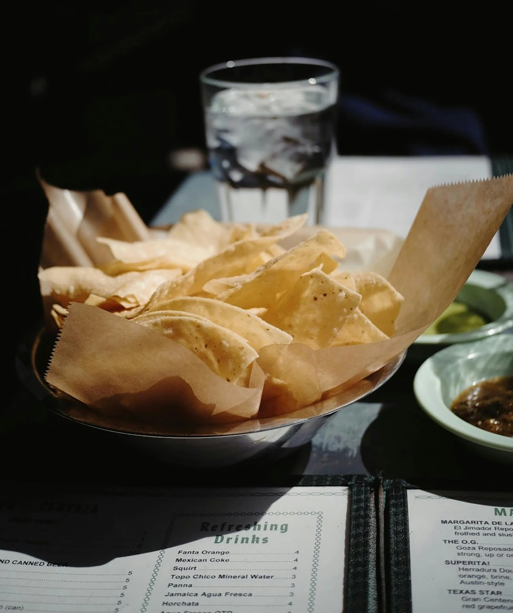 a silver plate with chips on a table next to a glass of water