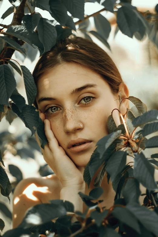 a woman holds her face against a leafy nch