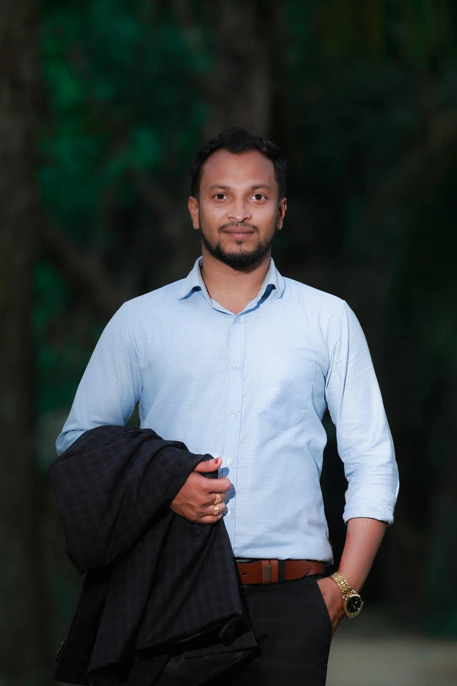 man in blue shirt standing near trees with bag