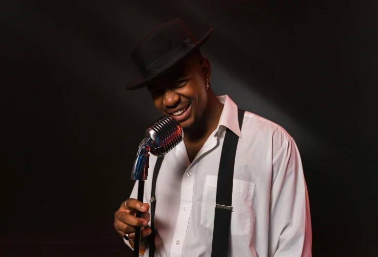 man in black hat, suspenders and white shirt sings into microphone