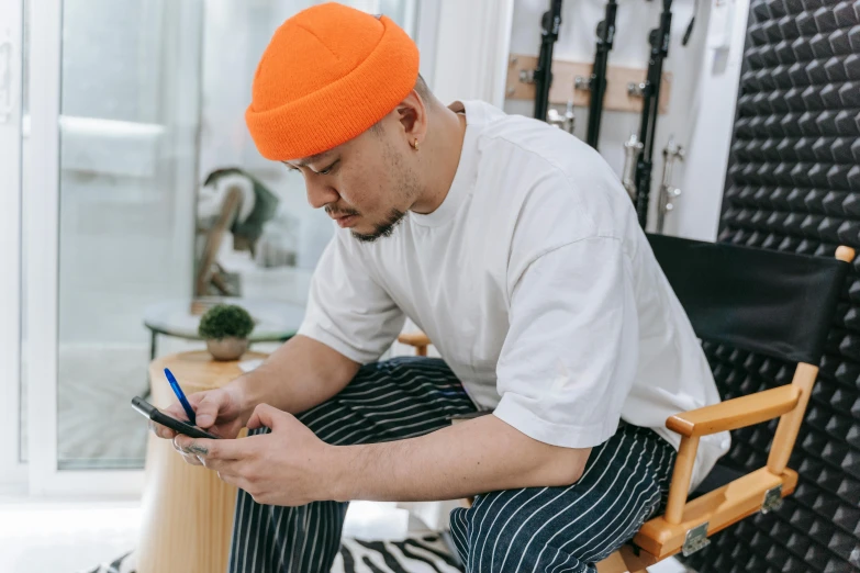 a man in an orange turban sits in a chair looking at his phone