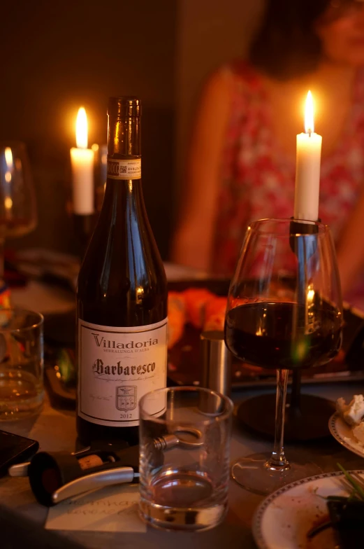 candles, a plate with food, glasses and bottles on a table