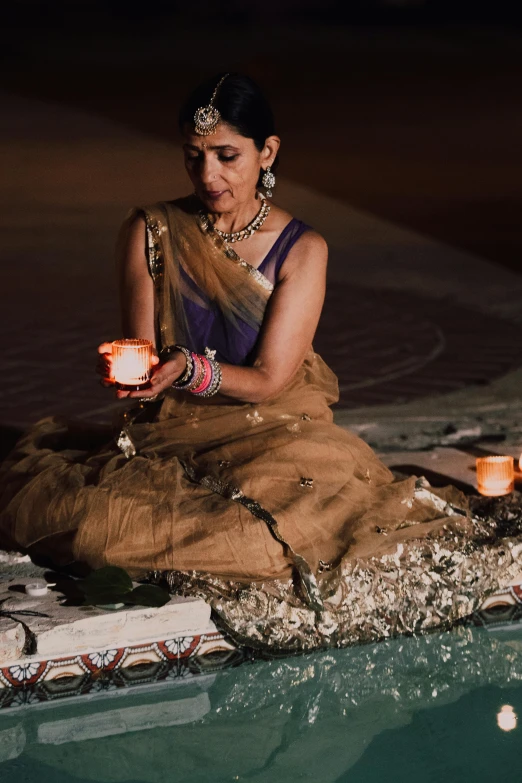 an indian woman sitting in a pool lit with candles