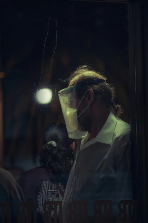 a man looking through a window with a protective mask on