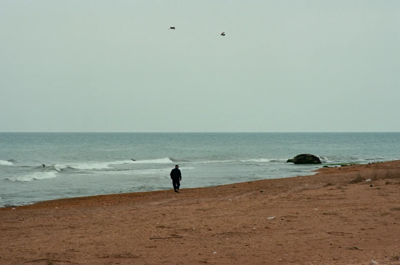 a person standing on the beach while a kite flies above