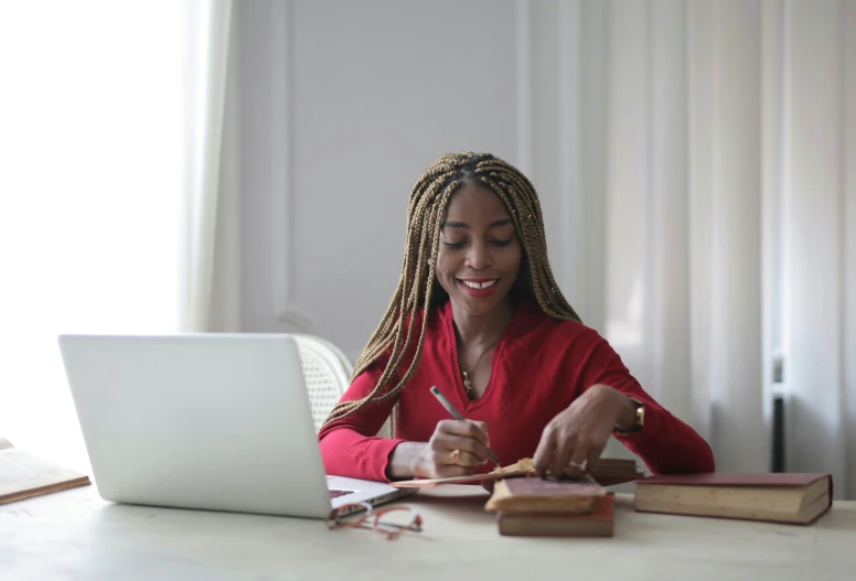 a woman sitting at her desk and writing in front of her laptop