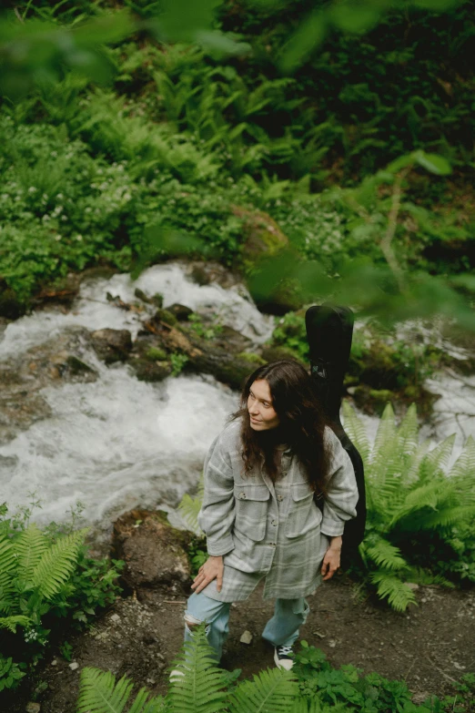 a woman standing next to a river in a lush green forest