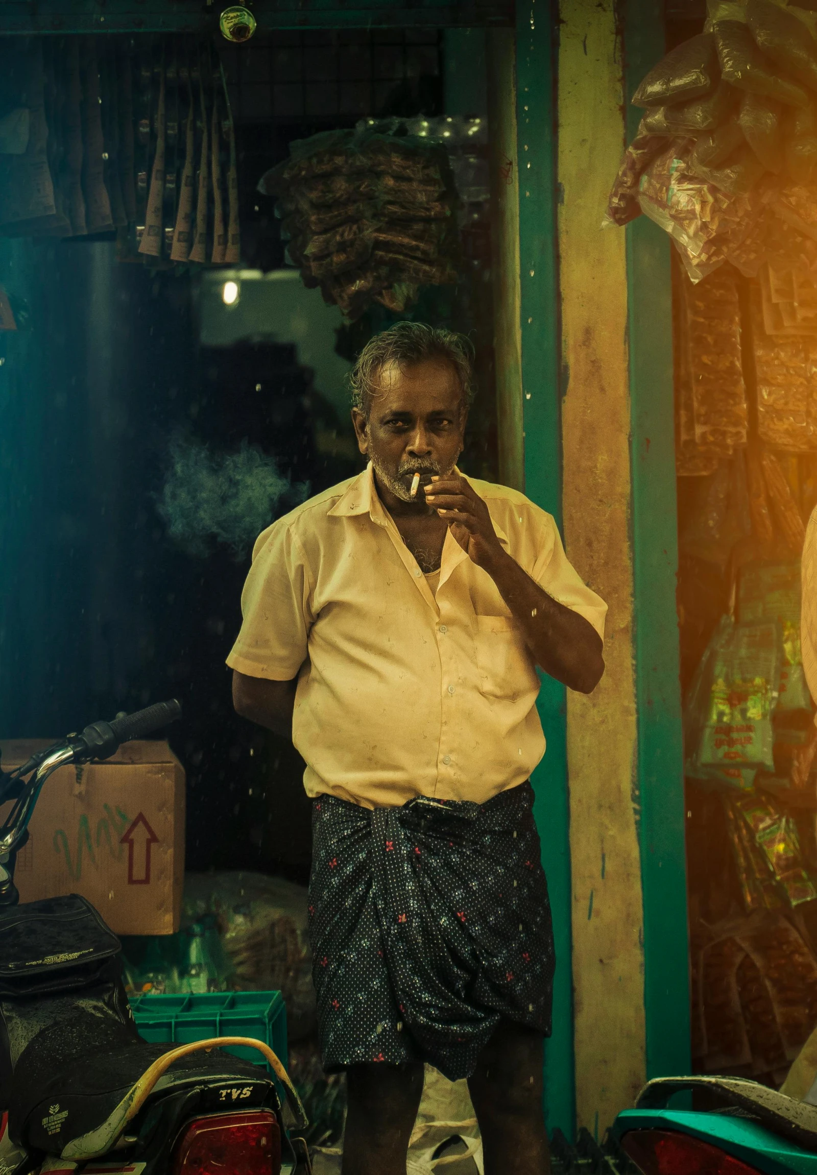 an elderly man is standing outside his shop smoking