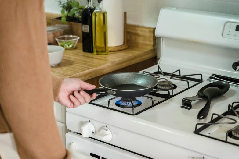 a person touching a small frying pan on the top of a stove