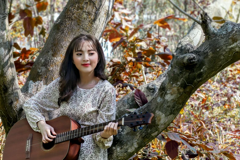 a woman wearing a white dress, holding an acoustic guitar sitting in a tree
