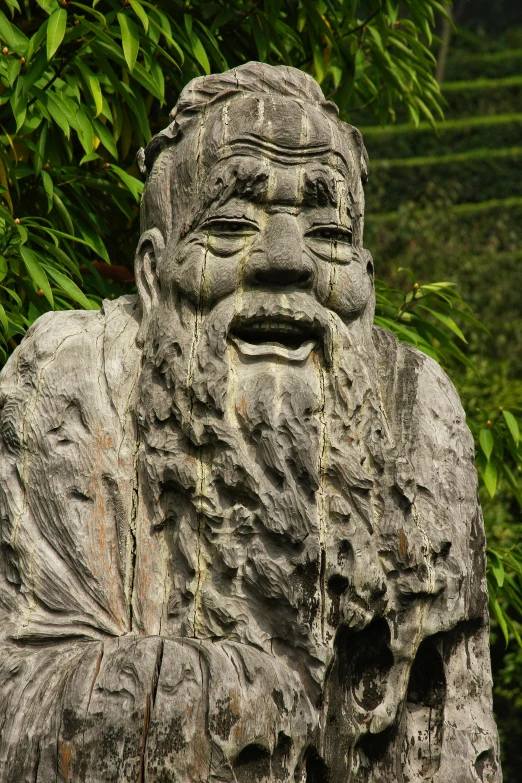 a statue with many faces, sitting in front of bushes
