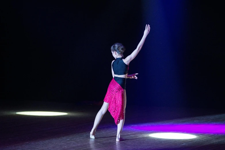 a ballerina with one leg raised is standing on a dance floor and lighting around her