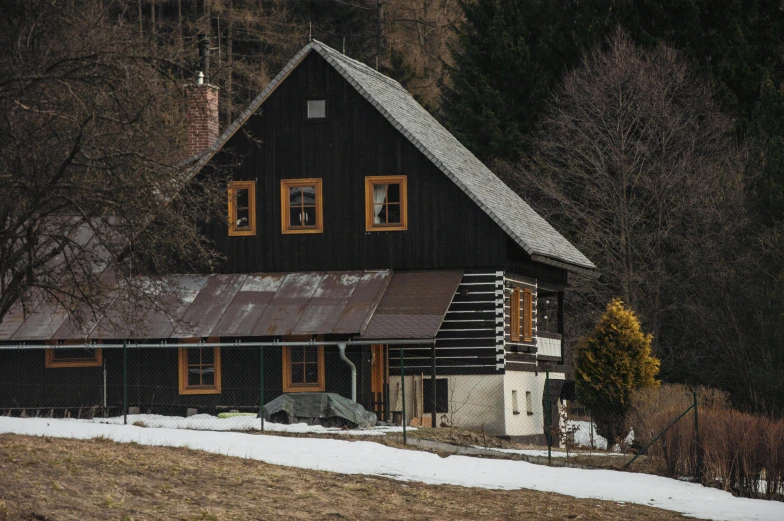 a black building with wood trim and two windows near some trees