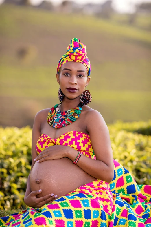 a pregnant woman in a bright colorful dress sits outside