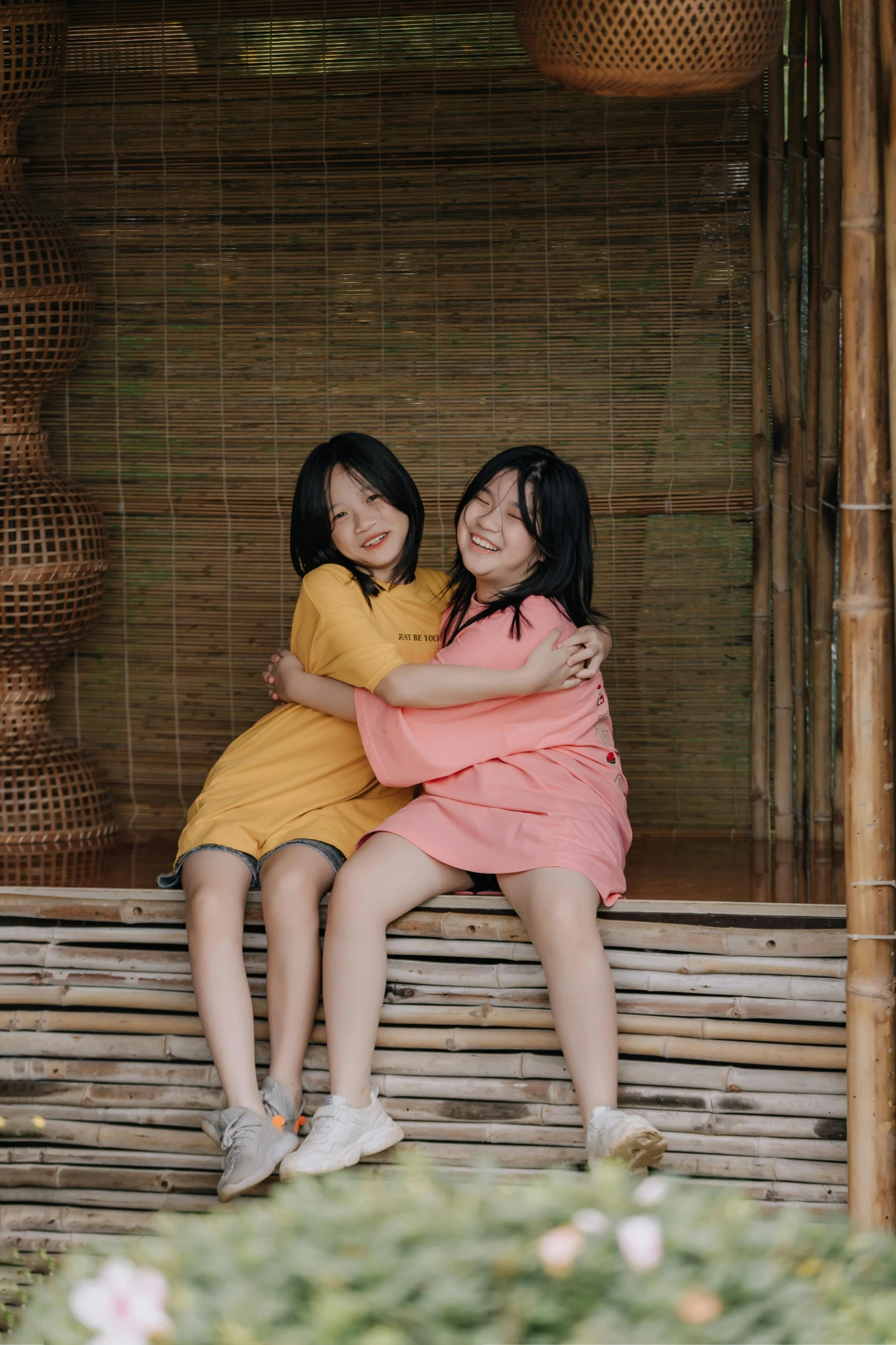 two women hugging on a wooden bench near the bamboo fence