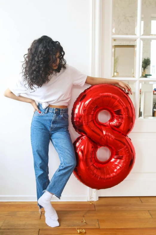 woman leaning on wall holding red balloon in shape of the number eight