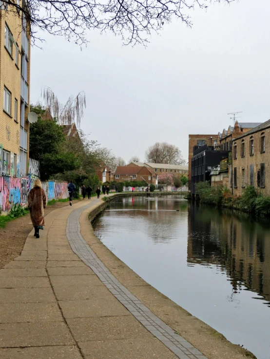 a woman walking down a path towards a river with graffiti on the wall