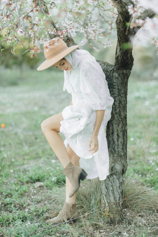 woman in white dress and hat sitting on tree's trunk