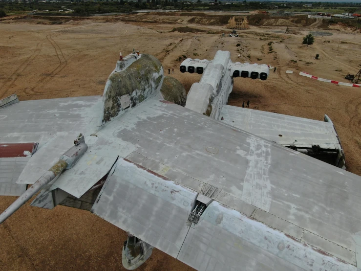 a abandoned airplane on top of dirt field next to trees