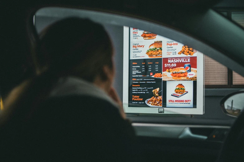 a man in a car looking at a large screen television