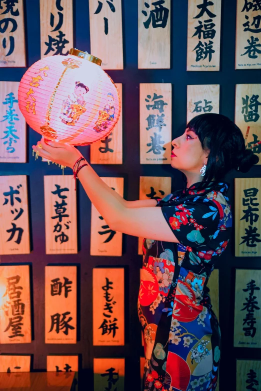 a person holding up a decorative lantern in front of wall with asian writing