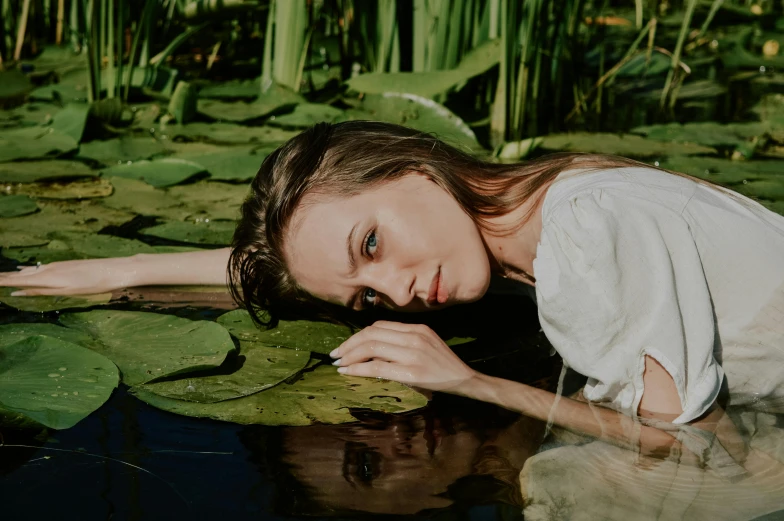 a woman is lying on top of the water in the middle of water lillies