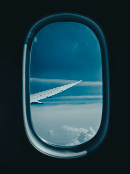 an airplane wing with a dark blue sky and clouds seen through the window