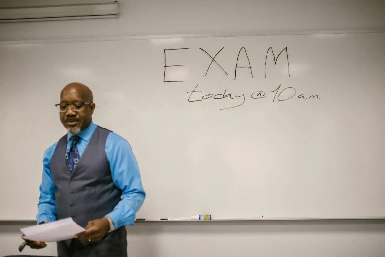 a man with glasses and a vest standing in front of a white board