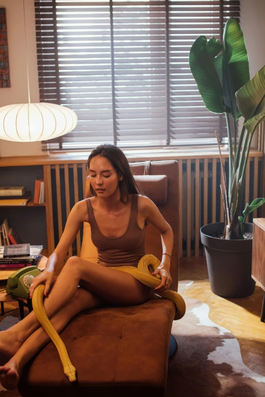 a woman sitting on a brown chair with a yellow banana in her hand