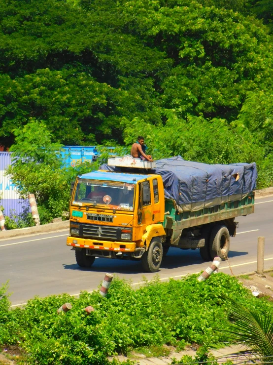 a yellow truck traveling down a street near trees