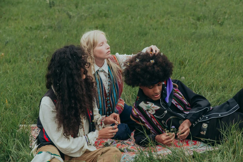 two girls and one boy sitting on a blanket in the grass