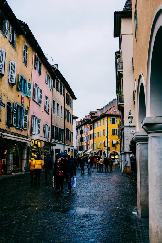 several people walking down a cobblestone street with buildings in the background