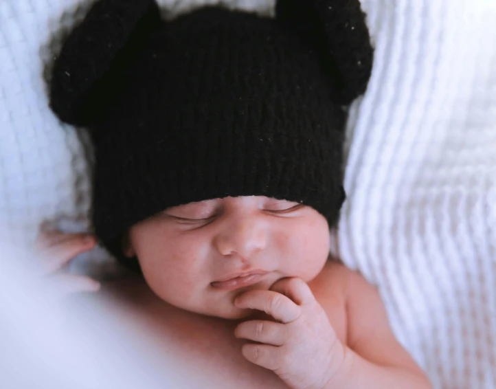 a baby sleeping with a black knit hat on top of it