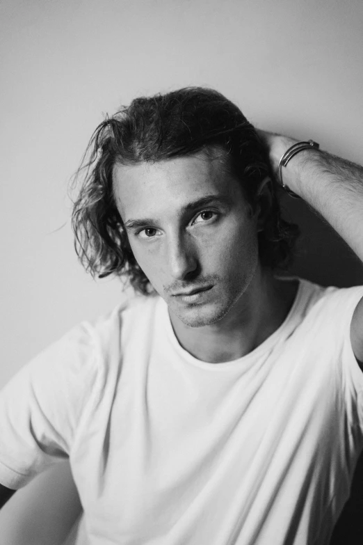 man in white tee shirt leaning on wall with his hand under his head