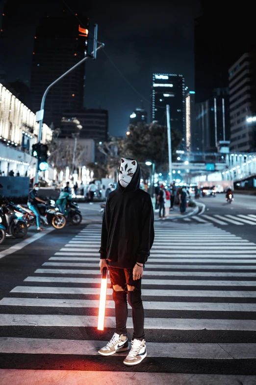 a guy wearing a mask is standing near a crosswalk at night