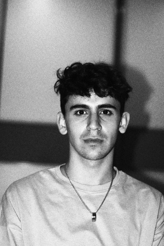 young man sitting in the middle of the room with a necklace on