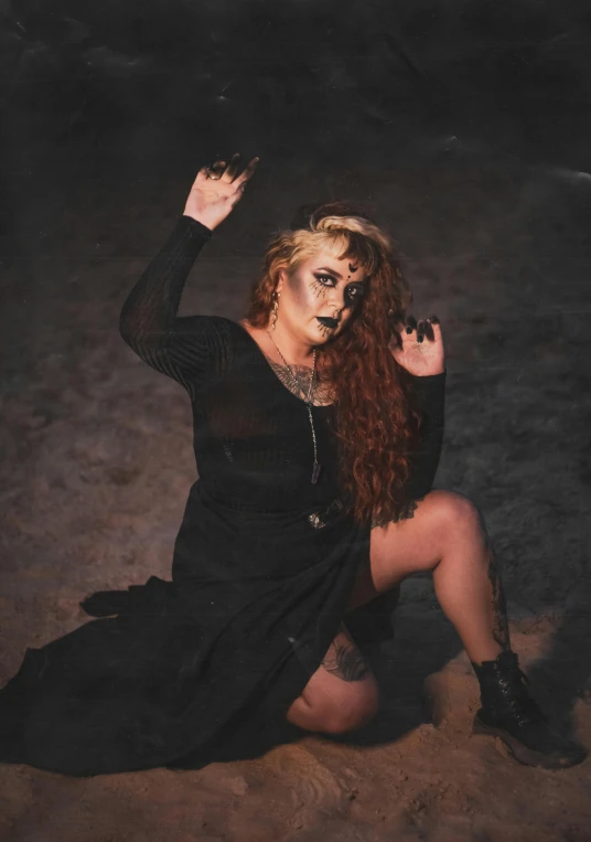 a woman with dark makeup on her face and long hair sitting in the dirt