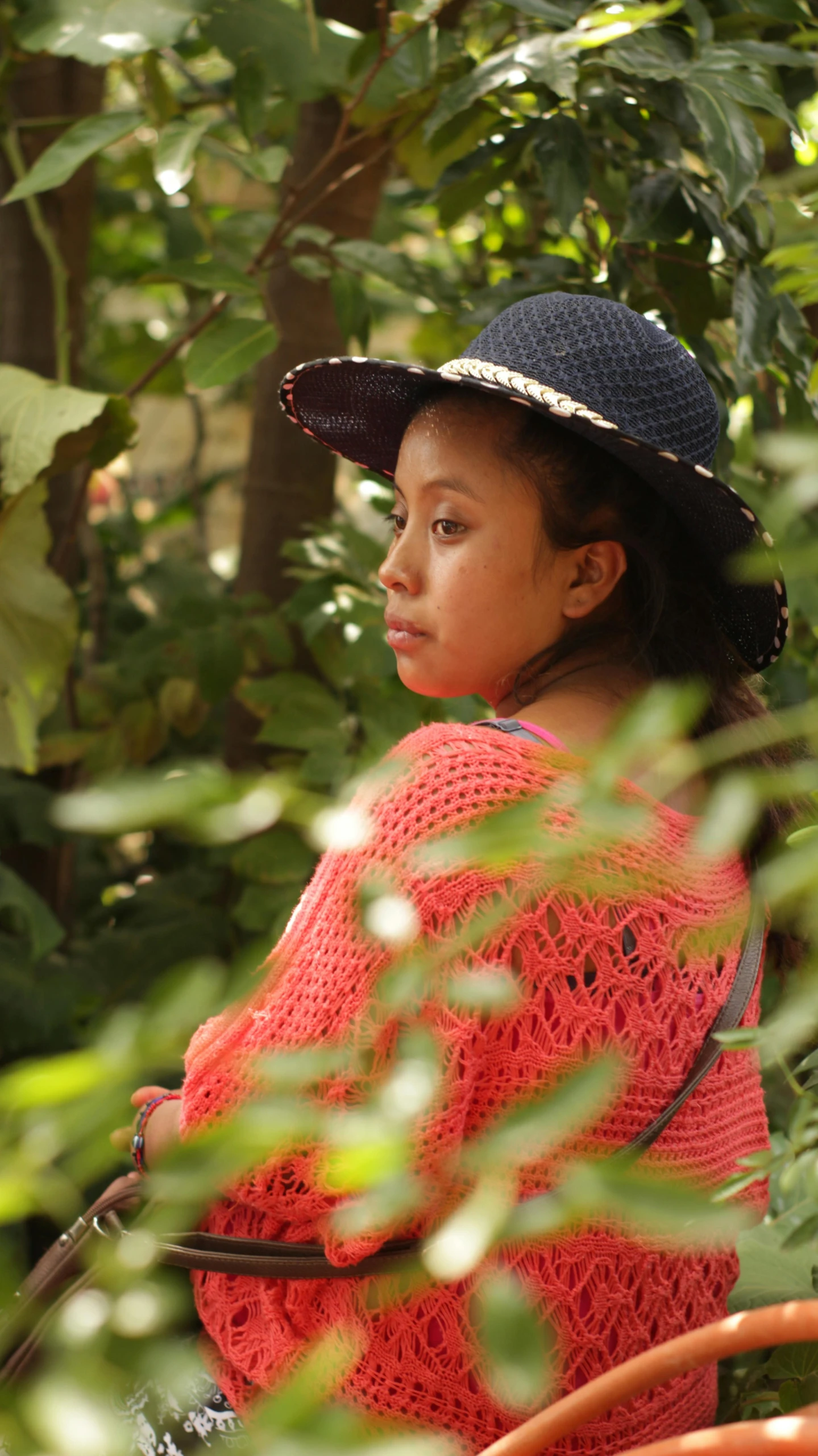 young woman in bright, red sweater, straw hat and black and orange handbag