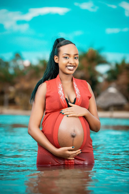 a pregnant woman wearing a red dress standing in a body of water