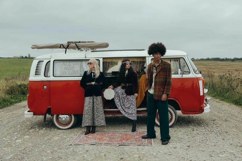 three hipsters stand near a mini van in the middle of the road