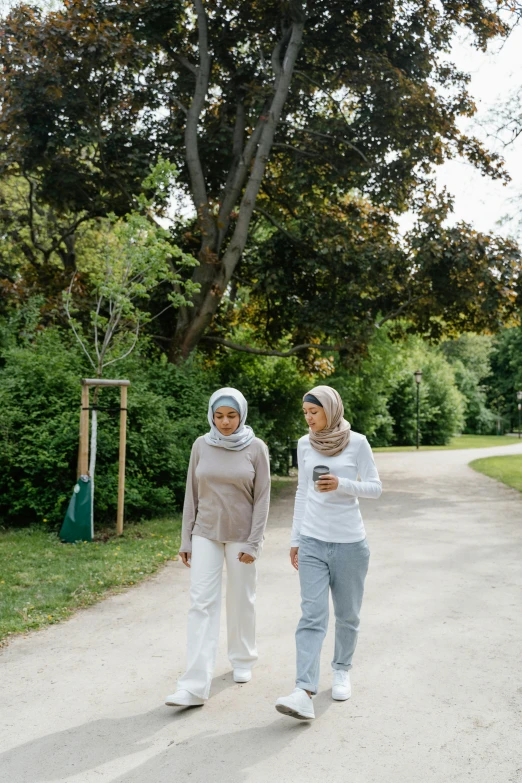 two woman walk in the park while using their cell phones