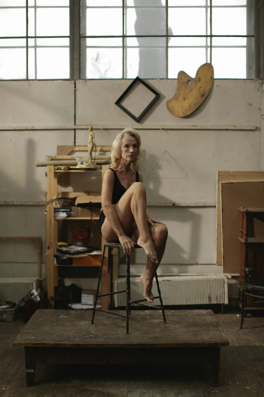 a blonde woman sits on a stool in the shape of a chair