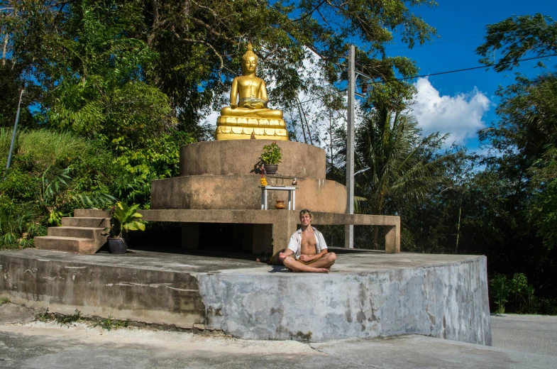 a man is sitting on the side of a building in front of a gold buddha statue