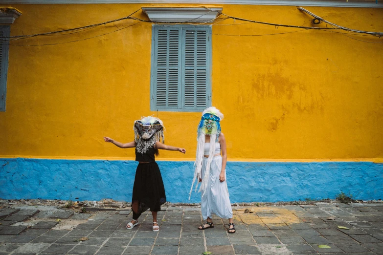 two girls in front of a yellow building wearing masks