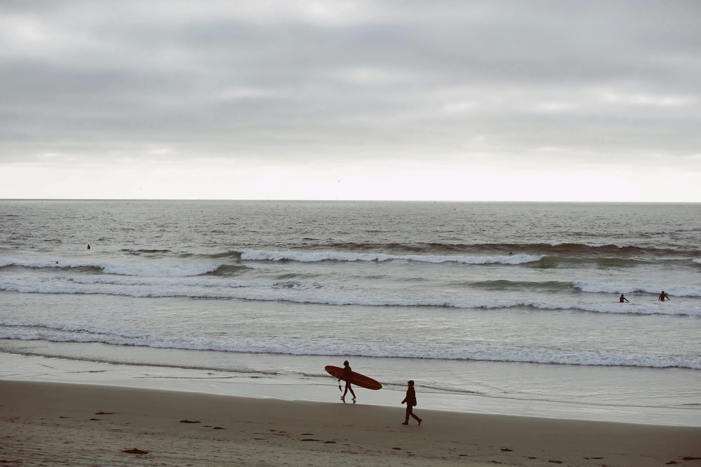 two people walk with a surf board towards the ocean