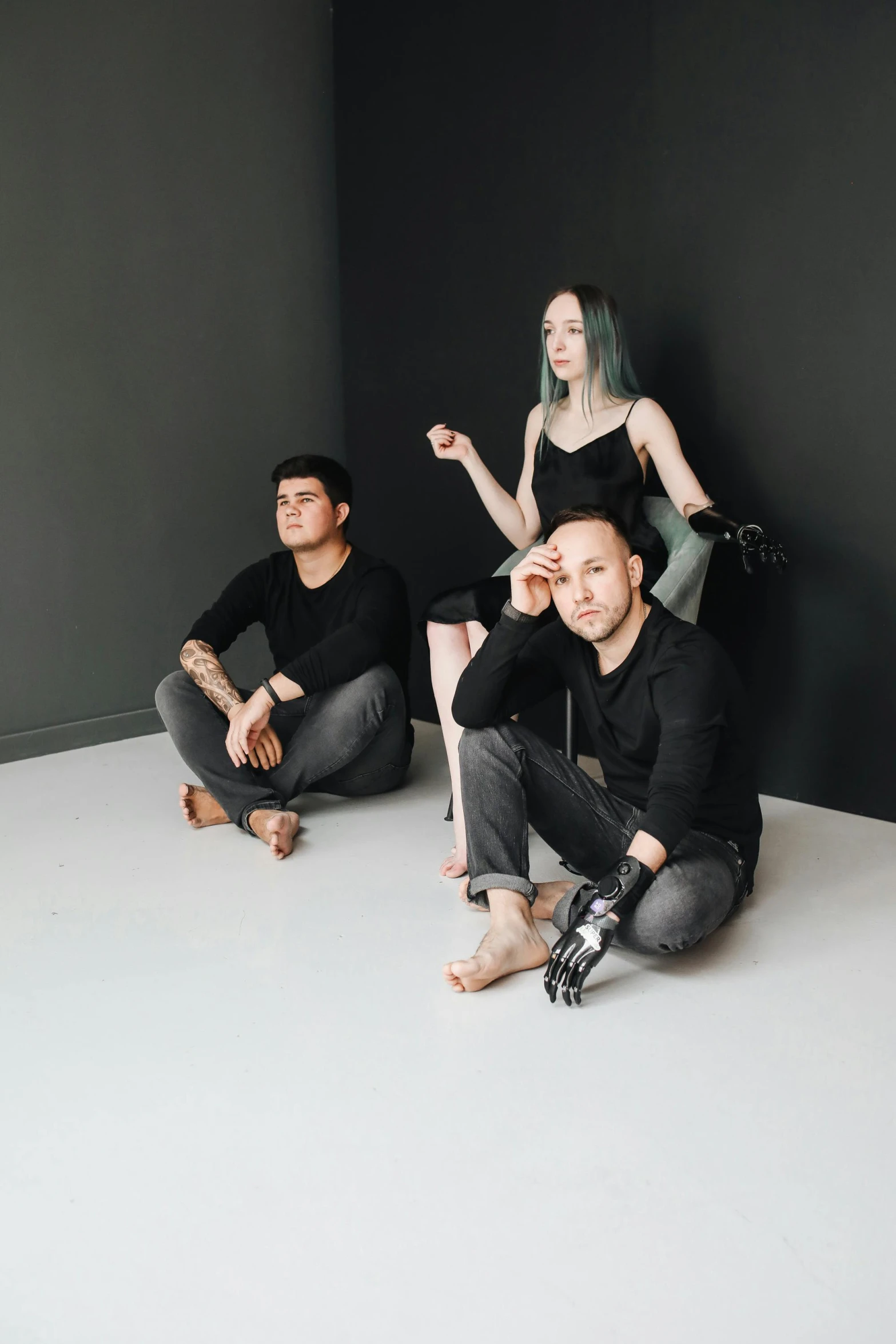 a group of three models wearing black sitting against a wall