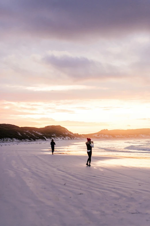 people are walking along the shore line while the sun is setting