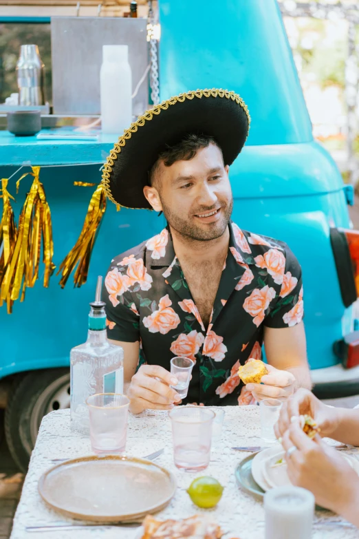 man eating an open sandwich at a table with a mexican hat on his head